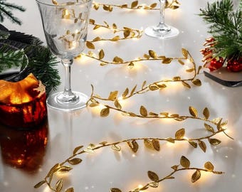 May include: Gold leaf garland with warm white LED lights. The garland is strung on a wire and has small, realistic-looking leaves. The garland is perfect for adding a touch of elegance to any space.