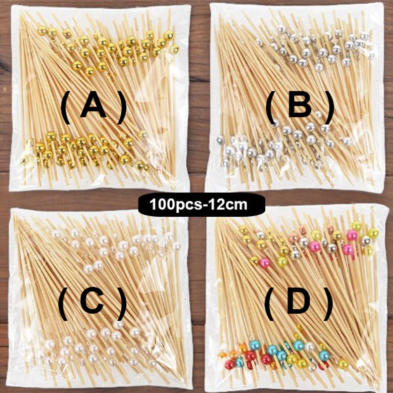 May include: Four bags of 100 bamboo skewers with decorative beads. The bags are labeled (A) through (D). Bag (A) has gold beads, bag (B) has silver beads, bag (C) has white beads, and bag (D) has multi-colored beads.
