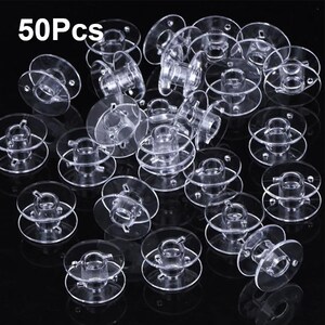 May include: A set of 50 clear plastic bobbins for sewing machines. The bobbins are stacked and scattered on a black background.