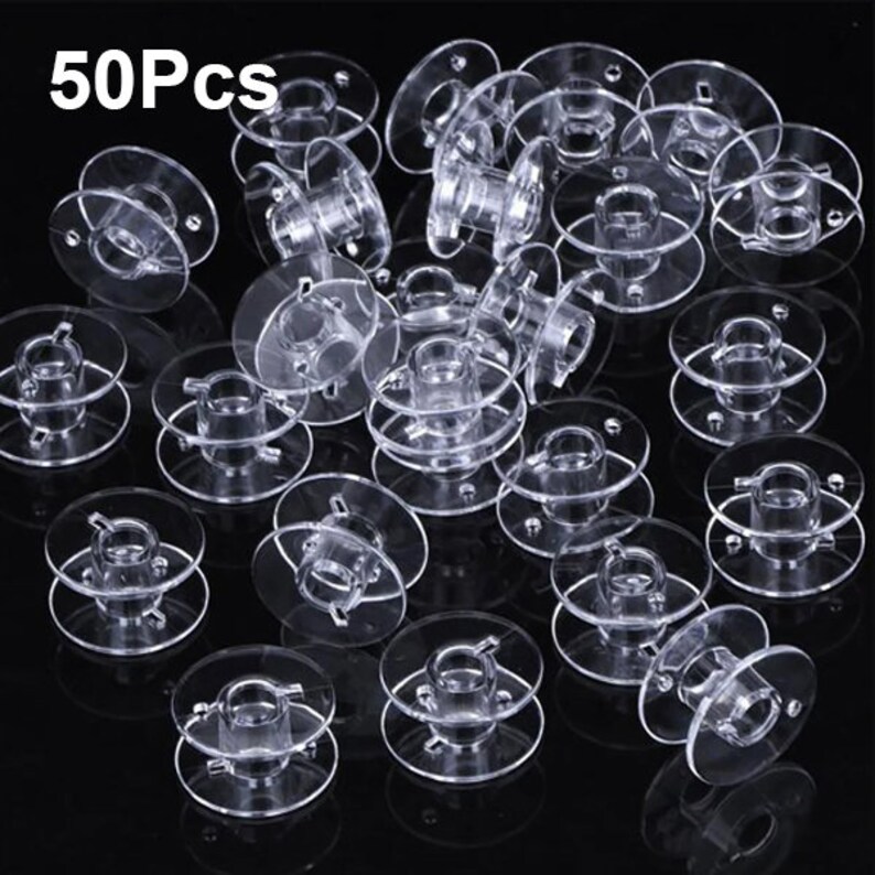 May include: A set of 50 clear plastic bobbins for sewing machines. The bobbins are stacked and scattered on a black background.