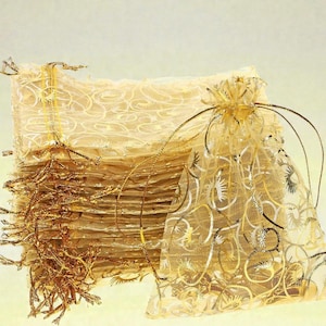 May include: A collection of sheer, gold-toned gift bags with a decorative, swirling pattern. One bag is open, revealing the contents. The bags are tied with gold string and have a delicate, elegant appearance, suitable for small gifts or favours.