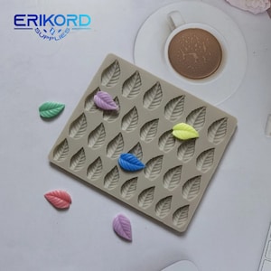 May include: A silicone leaf mold with multiple leaf impressions. Several colorful leaf-shaped candies in shades of pink, green, blue, and yellow are scattered around the mold. The logo "ERIKORD SUPPLIES" is visible in the top left corner.