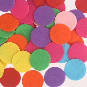 Op de afbeelding: Assortiment van vilt cirkels in verschillende kleuren, waaronder rood, oranje, geel, groen, blauw, paars en roze. De cirkels zijn allemaal even groot en zijn in een willekeurig patroon gerangschikt.