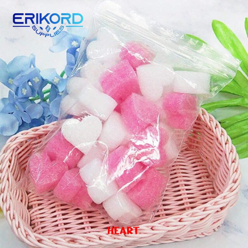 May include: A clear plastic bag filled with pink and white heart-shaped foam packing peanuts. The bag is sitting in a pink wicker basket. The text "HEART" is printed on the bottom of the basket.