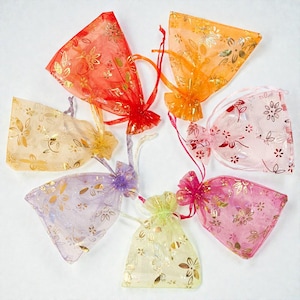 Op de afbeelding: Een verzameling kleurrijke organza cadeauzakjes. Elk zakje heeft een andere kleur, waaronder rood, oranje, roze, paars, geel en goud. De zakjes zijn versierd met gouden bloempatronen en vastgebonden met bijpassende linten.