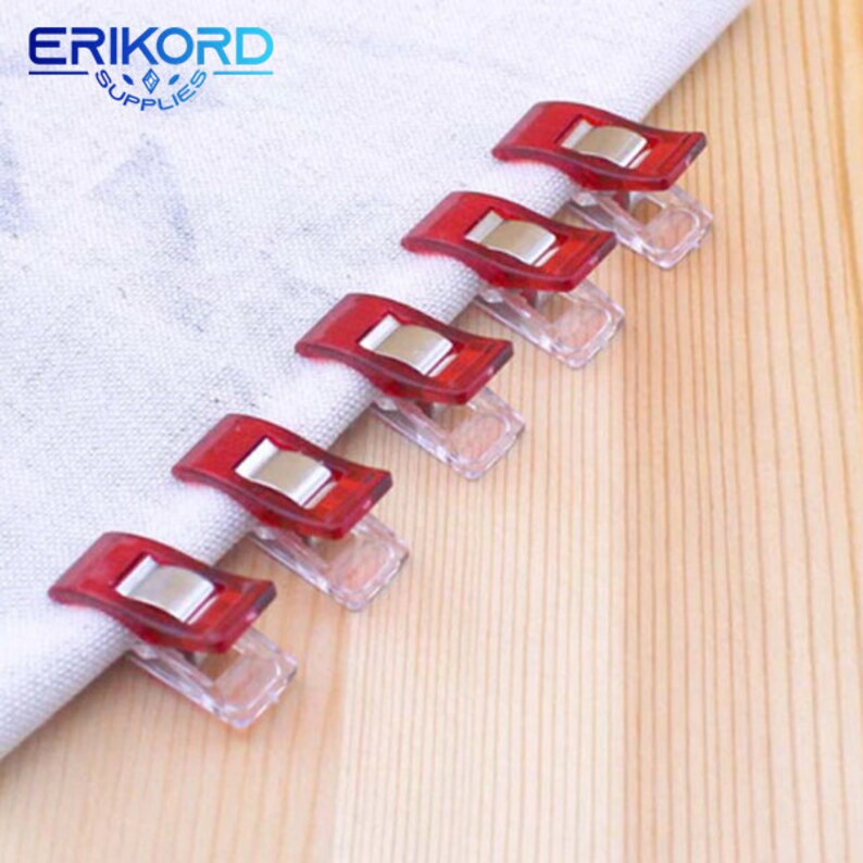 May include: Six red and clear plastic clips for sewing or quilting. The clips have a metal spring to hold fabric together.