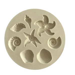May include: A silicone mould with eight different shapes of seashells and starfish. The mould is white and has a smooth surface.