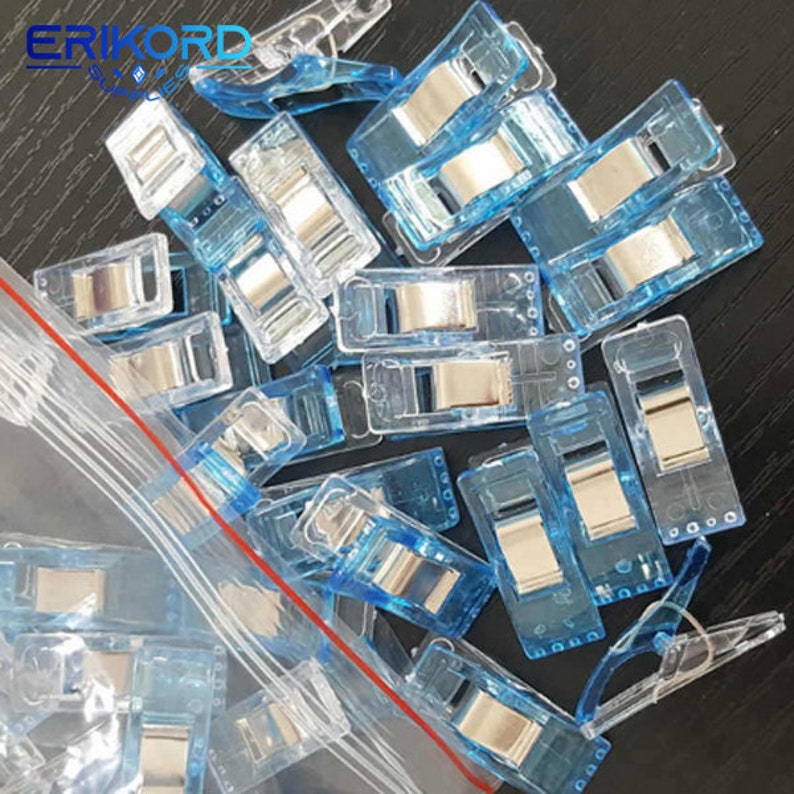 May include: A close-up of a pile of clear blue plastic clips with silver metal spring mechanisms. The clips are in a clear plastic bag with a red zipper.