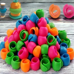 May include: A large pile of colorful yarn holders. The holders are made of plastic and are shaped like a spiral. They are in the colors green, blue, pink, and orange.