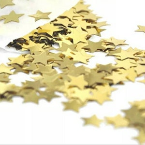Peut inclure: Un tas de confettis dorés en forme d'étoile. Les confettis sont éparpillés sur une surface blanche.