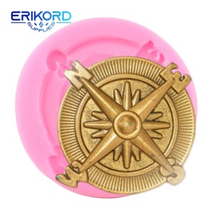 Könnte beinhalten: Rosa Silikonform mit einem goldenen Kompass-Design. Der Kompass hat einen Stern im Zentrum und die Buchstaben N, S, E und W am Rand.