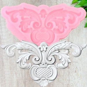 May include: A pink silicone mould shaped like a decorative floral design. The mould is used to create a decorative element for cakes, cookies, or other desserts.