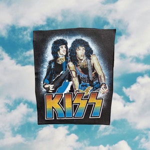 May include: A black fabric patch with a colorful KISS logo and an image of two musicians playing guitars.