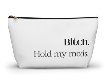 Può includere: Pochette cosmetica bianca con cerniera nera e la scritta "Bitch. Hold my meds." stampata in nero. La borsa è realizzata in materiale strutturato e ha una forma rettangolare.