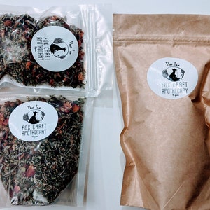 May include: Three clear plastic bags filled with dried herbs and flowers. Each bag has a white circular label with a black fox illustration and the text "Thar Tea Fox Craft Apothecary".