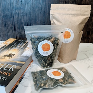 May include: Three clear plastic bags filled with loose leaf green tea. The bags are labeled with a round sticker that says "Fourteenth of the Hill Tea" and "Fox Craft Apothecary".
