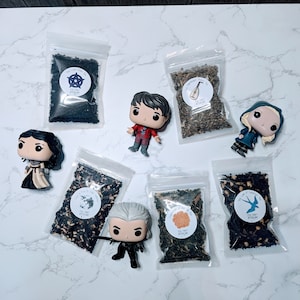 May include: Assortment of loose leaf tea blends in small bags with various character figurines. The tea blends include "The Last Unicorn", "The Voyage", "Flower of the Summer", and "The Song of Surprises".
