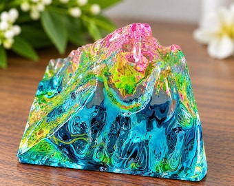 May include: A mountain-shaped sculpture made of clear resin featuring a vibrant, swirling marbled pattern of bright pink, neon green, and deep turquoise blue. The surface is smooth and glossy, reflecting light across its jagged, peak-like form.