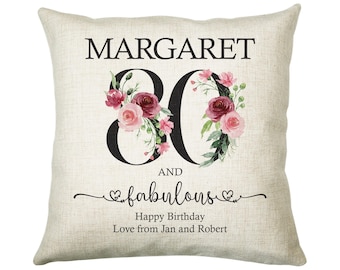 May include: A white linen pillow with the text "MARGARET 80 AND fabulous" in black. The number 80 is decorated with pink and burgundy watercolor flowers. The text "Happy Birthday Love from Jan and Robert" is also included.