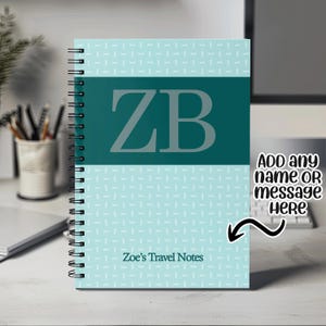 May include: A teal blue and white spiral bound notebook with the initials "ZB" in a large white font on the front cover. The notebook has a white and teal blue patterned design and the text "Zoe's Travel Notes" at the bottom of the cover.