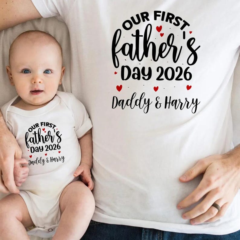 Op de afbeelding: Een witte romper en t-shirt set met de tekst "OUR FIRST Father's Day 2026 Daddy & Harry" in zwart script en rode hart accenten. De baby draagt de romper en de volwassene draagt het t-shirt.
