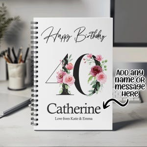 May include: A white spiral bound notebook with a floral design around the number 40. The text "Happy Birthday" is at the top of the notebook. The text "Catherine" is below the number 40. The text "Love from Katie & Emma" is below the name. The text "ADD any name OR message Here" is in the upper right corner of the notebook.