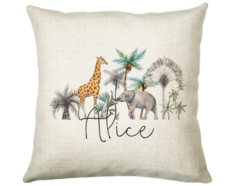 May include: A beige throw pillow with a watercolor illustration of a giraffe, elephant, and palm trees. The pillow has the name "Alice" written in black cursive.