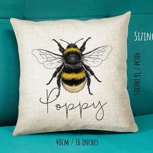 May include: A white throw pillow with a black and yellow bumblebee illustration and the word "Poppy" written in cursive. The pillow is 16 inches by 16 inches.
