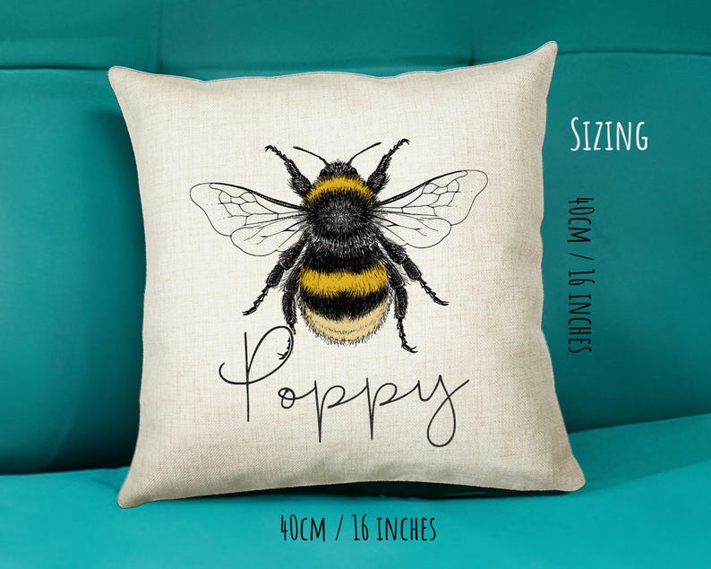 May include: A white throw pillow with a black and yellow bumblebee illustration and the word "Poppy" written in cursive. The pillow is 16 inches by 16 inches.