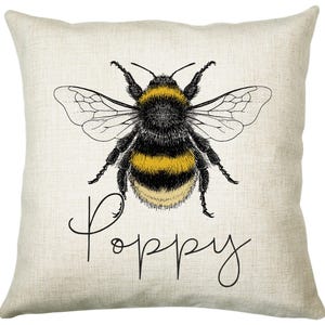 May include: A beige pillow with a black and yellow bumblebee illustration and the word "Poppy" in black cursive writing.