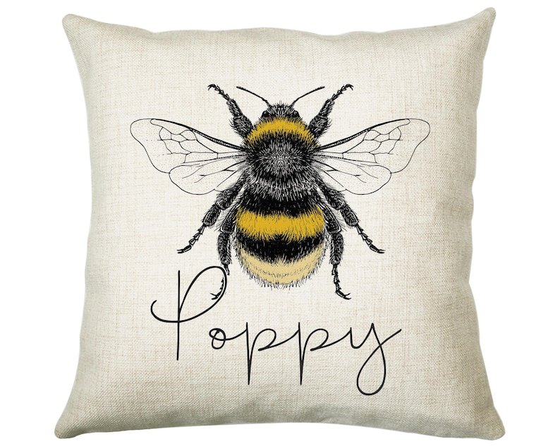 May include: A beige pillow with a black and yellow bumblebee illustration and the word "Poppy" in black cursive writing.