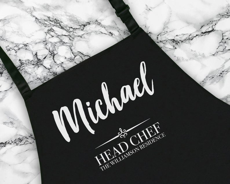 May include: Black apron with white text that reads "Michael Head Chef The Williamson Residence".