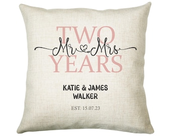 Może przedstawiać: Beżowa poduszka lniana z napisem "TWO Mr & Mrs YEARS" w różowych literach. Pod napisem znajduje się "KATIE & JAMES WALKER EST. 15.07.23" w czarnych literach.