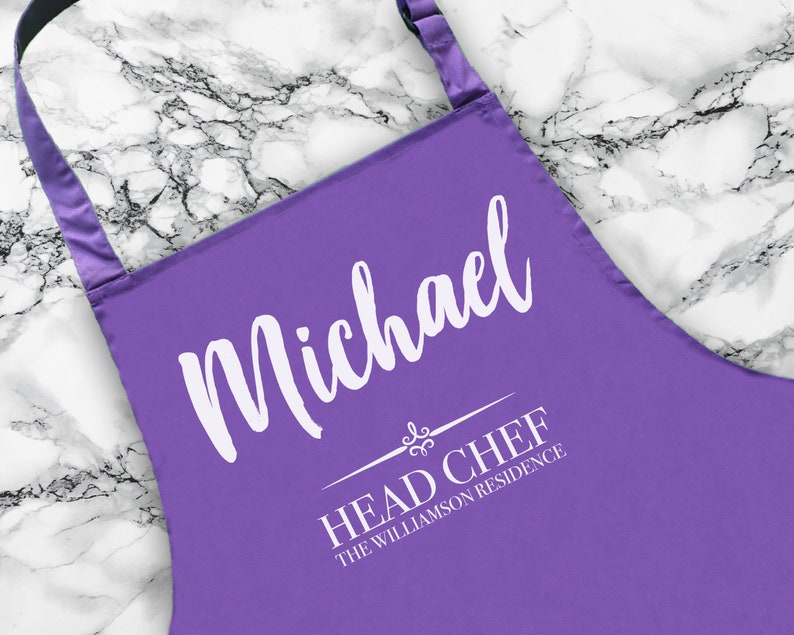 May include: Purple apron with white text that reads "Michael Head Chef The Williamson Residence".