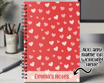 Może przedstawiać: Czerwony notes spiralny z wzorem różowych serc. Dolna część notesu ma różową wstążkę z tekstem "Emma's Notes". Tekst "ADD any name or wording here" znajduje się po prawej stronie notesu.