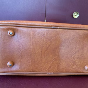 May include: A brown leather handbag with four silver metal feet on the bottom.