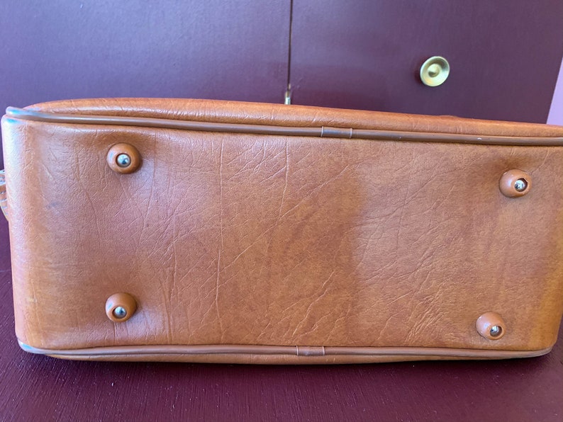 May include: A brown leather handbag with four silver metal feet on the bottom.