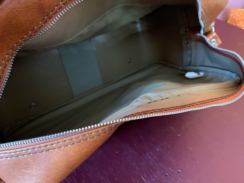 May include: The inside of a brown leather travel bag with a zipper closure. The bag is lined with a beige fabric.
