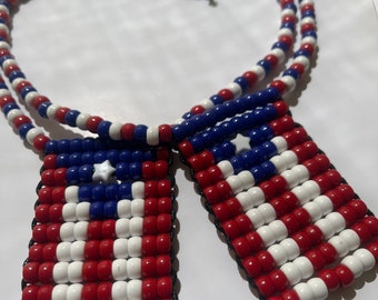 May include: A beaded necklace with two American flag pendants. The necklace is made of red, white, and blue beads. The pendants are made of the same beads and have a star in the blue field.