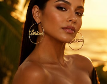 May include: A pair of large gold hoop earrings featuring the word Boricua written in a cursive script font across the center of each hoop. The earrings are circular in shape and made of a polished gold-toned metal material.