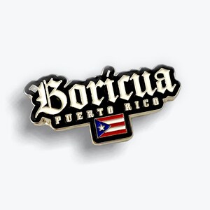 May include: A metal enamel pin featuring the word Boricua in a stylized white gothic font against a black background. Below the text, the words Puerto Rico appear in white, followed by a small rectangular Puerto Rican flag with red, white, and blue.
