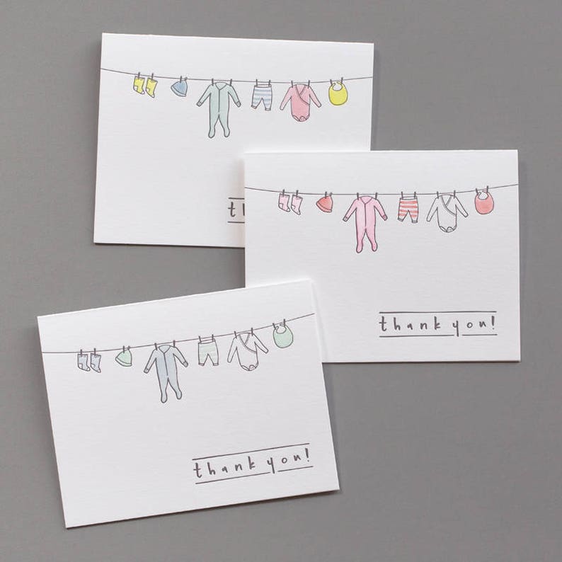 Puede incluir: Tres tarjetas de agradecimiento con una l&iacute;nea de ropa de beb&eacute; colgada en un tendedero. La ropa es de varios colores y patrones, incluyendo un body azul, un body rosa y un babero amarillo. Las tarjetas son blancas con texto negro que dice "&iexcl;gracias!"