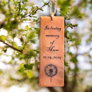 Puede incluir: Placa conmemorativa rectangular de color cobre con la inscripción "In loving memory of Mum" y la fecha "12.04.2025". Una ilustración de diente de león en la parte inferior. Colgante con un lazo de cuerda natural.