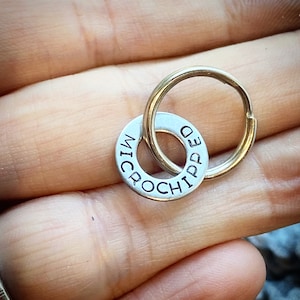 May include: A silver-colored, circular pet tag with the words "MICROCHIPPED" stamped around the edge, attached to a gold-colored key ring. The tag is designed to be attached to a pet's collar.