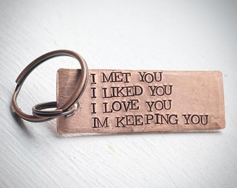 May include: A rectangular copper keychain with a split ring. The keychain has the following text stamped on it: "I MET YOU I LIKED YOU I LOVE YOU IM KEEPING YOU."