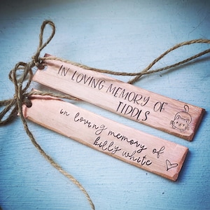 May include: Two rectangular copper tags with jute twine. One tag reads "IN LOVING MEMORY OF TIDDLS" with a cat illustration. The other tag reads "in loving memory of billy white" with a heart symbol.
