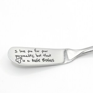 Puede incluir: Un cuchillo de mantequilla de acero inoxidable con una hoja curva. La hoja está grabada con la frase "I love you for your personality, but that is a HUGE BONUS."
