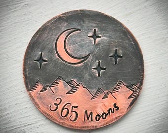 Op de afbeelding: Een ronde, koperkleurige hanger met een nachthemelontwerp. De hanger heeft een halve maan, sterren en bergsilhouetten. De tekst "365 Moons" is onder de bergen geëtst.