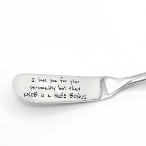 May include: A stainless steel butter knife with a curved handle and a wide, flat blade. The blade features black handwritten text that reads, "I love you for your personality but that knob is a HUGE BONUS."