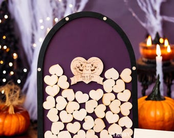 May include: A purple and black wooden guest book with a skull and crossbones design. The text "Till Death Do Us Part" is engraved on the heart-shaped sign. The sign also includes the names "Doug & Chris" and the date "October 11, 2018".